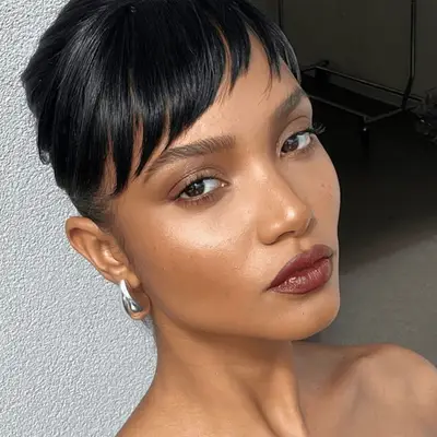 Model with very sharp and precise eyebrows, glowy makeup, and wearing dark lipstick. 