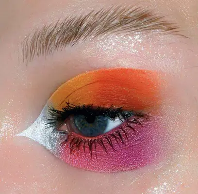 eye is shown wearing neon graphic makeup in neon orange, pink and silver tones