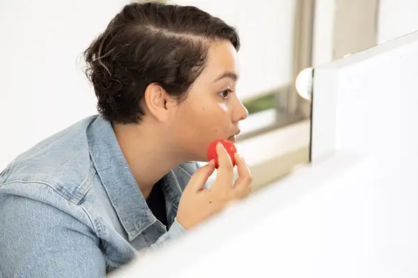 Person looking in mirror while using a makeup sponge to apply skin tint to their face