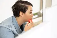 Person looking in mirror while using a makeup sponge to apply skin tint to their face