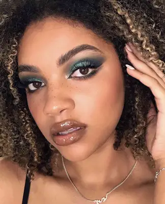 model wears shimmering green eyeshadow with glossy nude lips and visible freckles