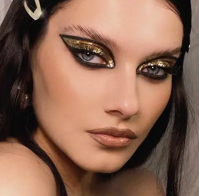 Model is wearing gold sparkly eyeshadow on the lid with black liner outliner the shape of a wing