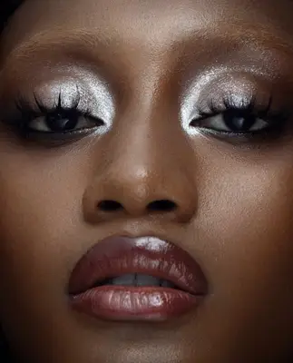 Model is wearing sheer silver eyeshadow all over the eyes with false eyelashes that are long and separated 