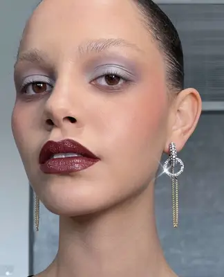 Model is wearing light grey eyeshadow with a deep bordeaux colored lipstick