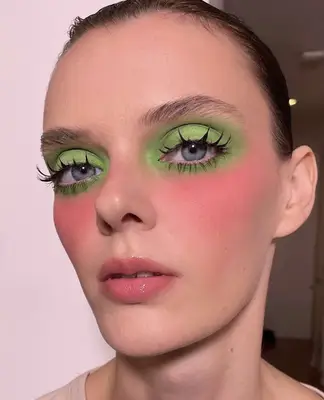 Model is wearing lime green eyeshadow with visible pink blush and eyelashes that are long and spider-like