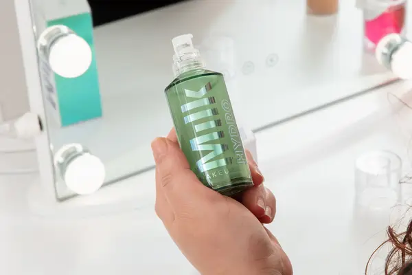 Person holding a bottle of Milk Makeup Hydro Grip Hydrating Makeup Primer in front of a mirror