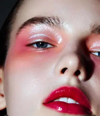 model is wearing a champagne glittery eyeshadow look with pink blush applied around the outer corner