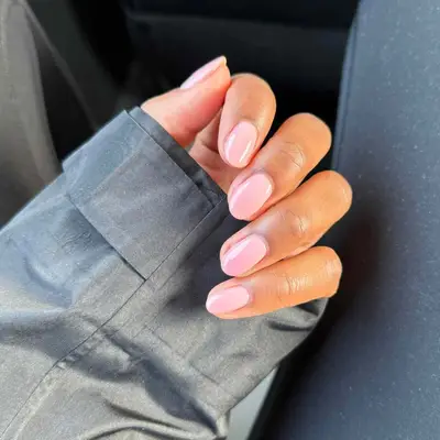 A hand resting on a dark fabric sleeve with short light pink manicured nails