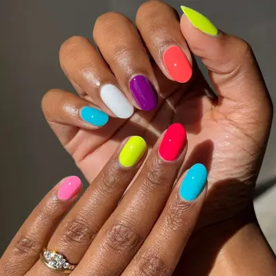 Hands displaying nails painted in a variety of bright colors, wearing a ring on one finger