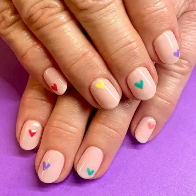 Close-up of hands with nail art featuring small heart designs in various colors on a purple surface