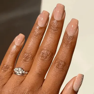 Hand with nude glitter manicure and a ring on the ring finger, nails are neatly styled