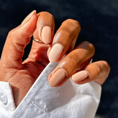 A hand with different colored nude manicured nails held against a dark background