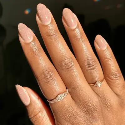 A hand with manicured nude glitter nails, wearing two rings
