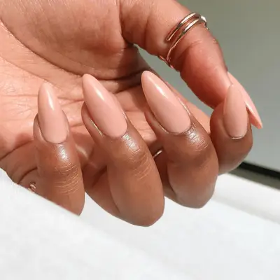 A hand displaying long almond-shaped nude nails with a smooth matte finish