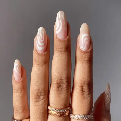 A hand wearing rings with bare manicured nails featuring a wavy design