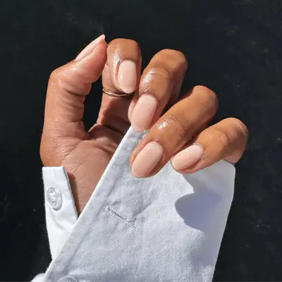 A hand wearing a white sleeve is shown with neatly manicured nails held against a dark background