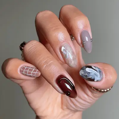 A hand displaying various styles of nail art in shades of nude