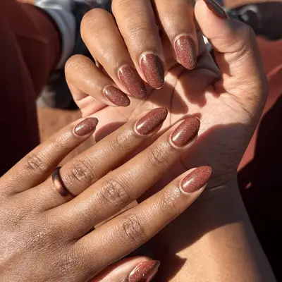 Manicured hands with brown nail polish and glitter holding each other, showcasing nail design