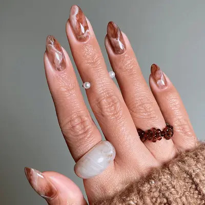 A hand displaying neutral marble nail art and wearing rings
