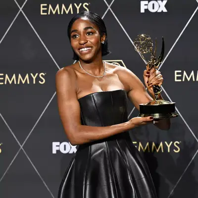 Alo Edebiri holding her Emmy Award wearing dark red, black cherry nails