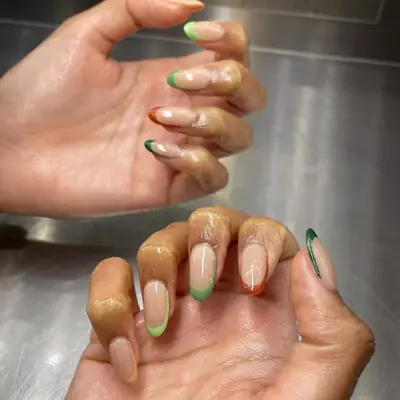 close up of nails painted in french tips with each nail in different earth tone color (greens and orange)