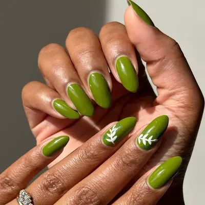 close up of nails painted in olive green shade with white leaf design on two fingers