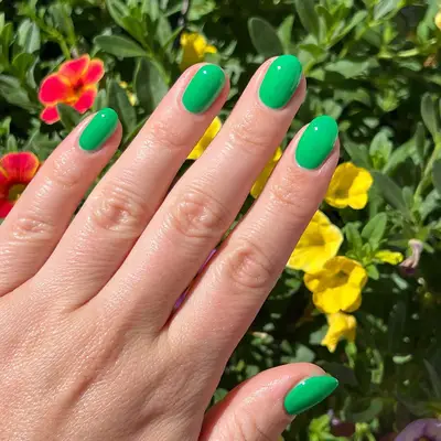 A short kelly green manicure with flowers in the background