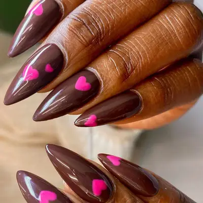 Close up of a glossy brown manicure with pink heart accents