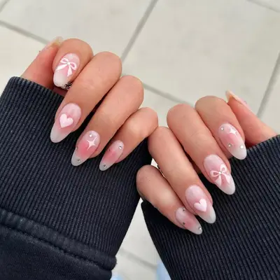 Coquette millennial pink manicure with starburst, hearts, and ribbons.