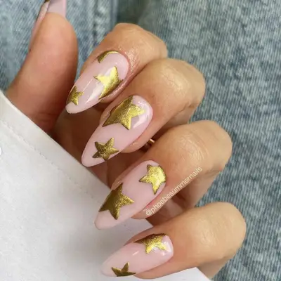 A manicure with a neutral pink base topped with gold stars