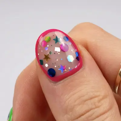 A thumb with encapsulated confetti, framed with pink polish