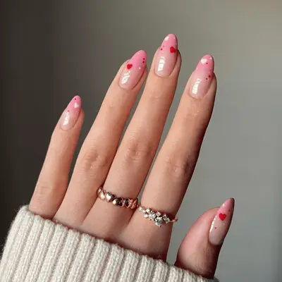 Closeup of oval nails with pink ombre tips and red and white heart designs.