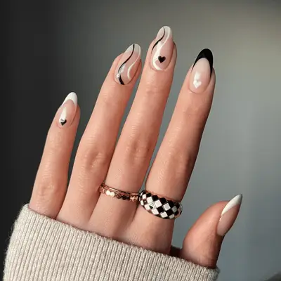 Nude nails with black and white swirl and heart designs.