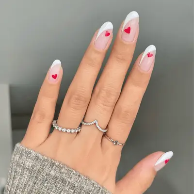 Long oval nails with an extended white French tip swoop and red heart details.