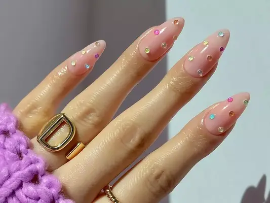 a strawberry milk manicure topped with gemstones