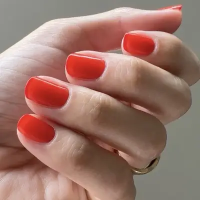 A hand with short, well-manicured nails painted in a bright color