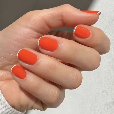 A hand showcasing shiny, well-groomed nails painted with a vivid orange polish, visible sunlight illuminating the detail