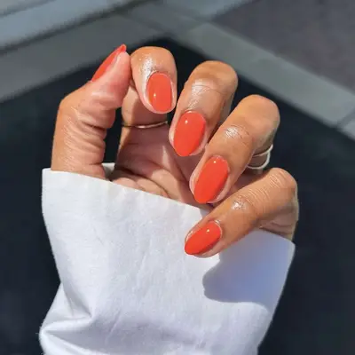 A hand with neatly manicured nails, painted bright orange, visible under natural light
