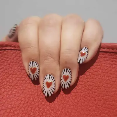 A hand with decorative heart-themed nail art resting on a red surface
