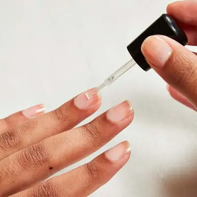 Close up of a woman using one hand to apply base coat to the nails on the other.