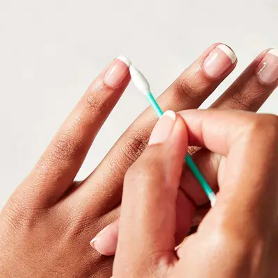 Woman uses a cotton swab to shape up French tips.