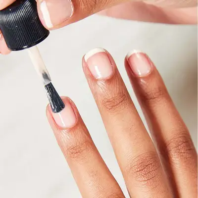 Woman adds a sheer pink coat of polish to her fingernail.