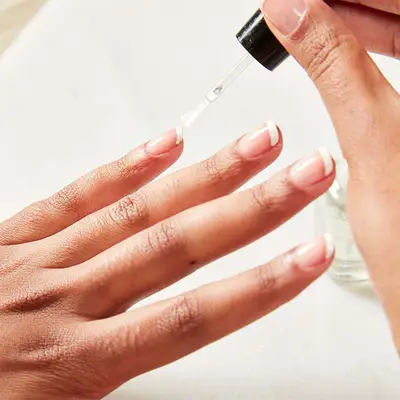 Woman applies top coat to her manicured hand.