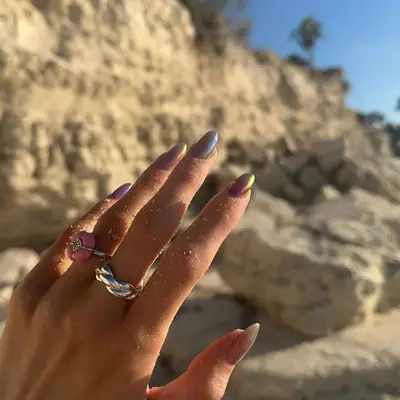 Hand in front of rocky landscape with nails of different colors with chrome 