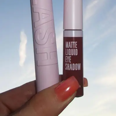 Jelly coral colored nails on hands holding two makeup tubes