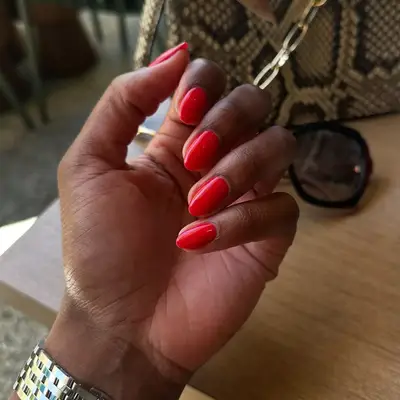 tomato red manicure with purse and sunglasses in background