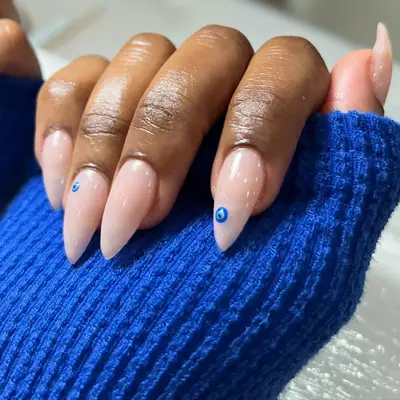 Hands curled into palm covered by blue sweater with milky nails that have evil eye designs