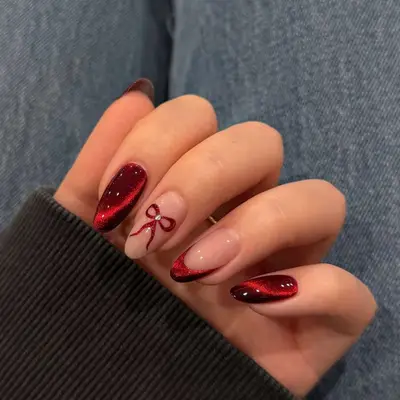 Ruby red velvet manicure with one French nail and one nail with a bow decal.