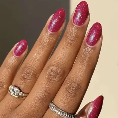 A hand with polished fingernails and rings on fingers, smooth red glittery nails