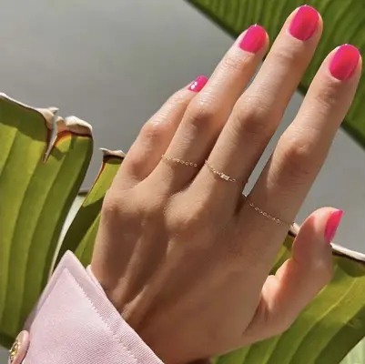 A manicured hand wearing delicate rings placed against green leaves